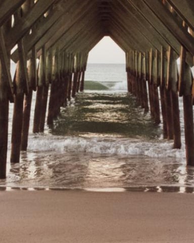 Wooden pier pilings extending into ocean waves and sandy beach