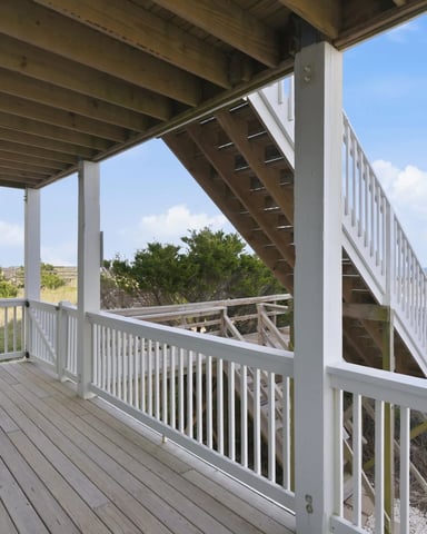 Covered deck with white railings and Adirondack chairs overlooking coastal dunes and ocean view