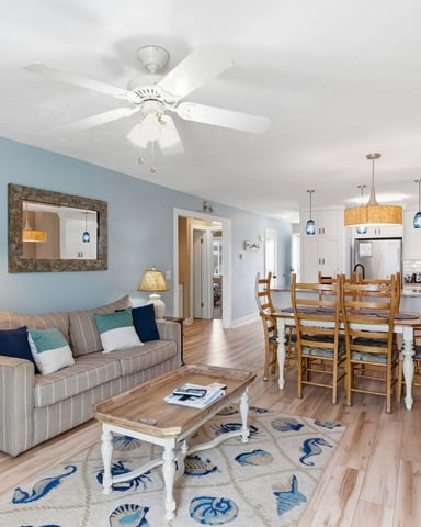 Open-plan living room and kitchen with blue accent wall, striped sofa, dining table, and white ceiling fan