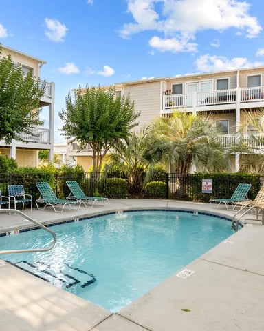 Residential pool area with lounge chairs, surrounded by multi-story vacation rental buildings and tropical landscaping