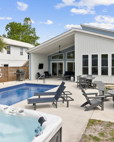 Modern white house with pool, hot tub, lounge chairs, and covered patio overlooking backyard