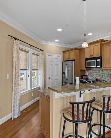 Kitchen with wood cabinetry, granite countertop island, black bar stools, and mosaic tile backsplash