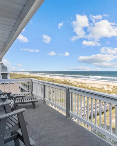 Oceanfront deck with Adirondack chairs overlooking sandy beach, dunes, and Atlantic Ocean under blue sky