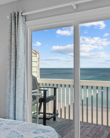 Bedroom with glass doors opening to oceanfront deck with Adirondack chair and beach view