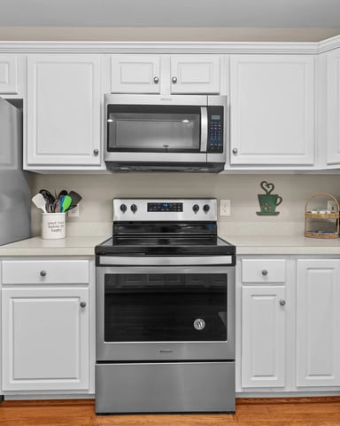Modern kitchen with white cabinetry, stainless steel appliances, beige countertops, and wood flooring