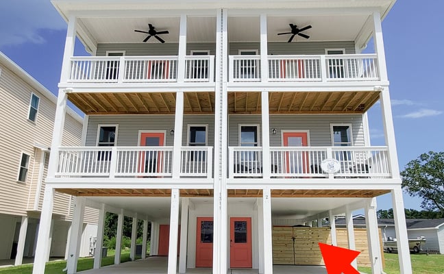 Modern three-story beach house with white exterior, red doors, multiple decks, and open ground-level carport